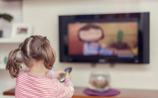 A child sitting alone on a sofa, engaged in screen time, watching cartoons on a television